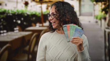 Malezya sirkesi banknotları tutan bir kadın açık hava restoranının terasında süveter ve gözlük takmış, finansal bir servet ya da heyecan öneriyor..