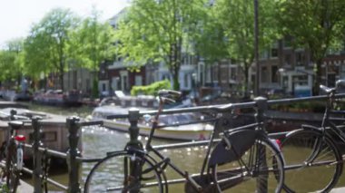 Arka planda Amsterdam 'ın ikonik kanalları ve bulanık kanal evleri olan bir tırabzanda dinlenen bisikletler cazibe ve sükunetle dolu klasik bir Avrupa kentsel manzarası yaratıyor..