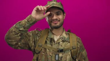 Stüdyoda kamuflaj üniforması giyen ve şapka takan İspanyol asıllı genç bir adam..
