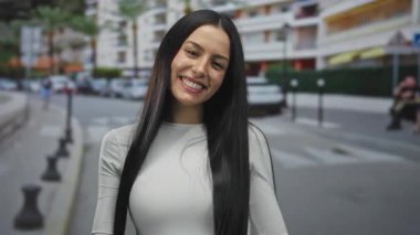 Şehir binaları ve arabalarla çevrili kalabalık bir caddede gülümseyen kadın neşeli bir ifadeyle canlı bir şehir atmosferini yakalıyor..
