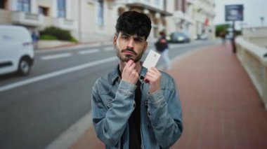 Kot ceketli genç adam, arka planı bulanık, şehir yaşam tarzını ve modern kimlik kavramlarını gösteren bir kart tutuyor..