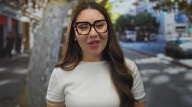 Beyaz gömlek giyen ve gözlüklü bir kadın gülümserken iki eliyle yanaklarına dokunuyor..