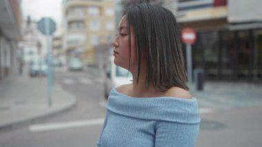 Şehir caddesinde mavi süveter giyen kadın sakin tavırları ve kapalı gözleriyle şehir mimarisi arasında gençlik huzurunu gösteriyor..