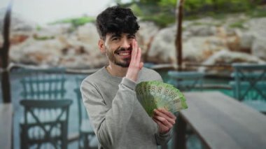 Elinde Rus rublesi tutan bir adam açık terasta restoran dekoruyla fısıldıyor, oyuncu ve yakışıklı görünüyor, elinde para ile sokak atmosferini yakalıyor..