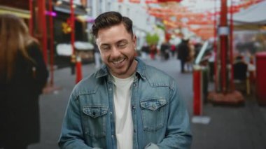 Kot ceketli, sakallı, gülümseyen ve hareketli şehir caddesinde yüzlerini kapatan genç bir adam..