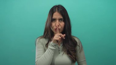 Yeşil izole bir zemin üzerinde dudakları üzerinde sessizce el kol gezen bir kadın anlamlı gözleri ve uzun koyu renk saçları olan gizemli bir mesaj iletiyor..