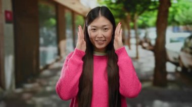 Pembe kazaklı kadın ağaçlarla şehir caddesinde dikiliyor. Rahat ve neşeli görünüyor. Açık havada modern şehir yaşam tarzını somutlaştırıyor..