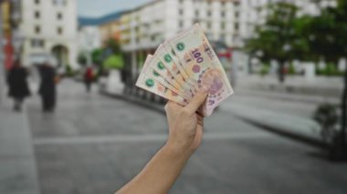 Arjantin pesolarını açık havada elinde tutan bir adam şehir ortamında para ve finans gösterisi yapıyor..