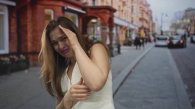 Tuğla dükkanlarıyla dolu kalabalık bir caddede elini yüzünü örten beyaz elbiseli kadın. Üzüntü kederi..