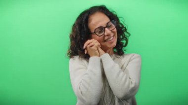 İzole edilmiş yeşil bir arka planda kıvırcık saçlı, neşeli ve dostane bir ifade yakalayan olgun bir kadın..