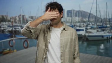 İspanyol adam güneşli limanda yüzlerini botlar ve dağ zeminiyle örtüyor, ekose gömlek giyiyor, deniz manzarasını çağrıştırıyor ve iç gözlem yapıyor..