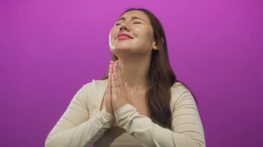 Elleri sımsıkı bağlı genç bir kadın stüdyoda canlı mor arka plana karşı dua ediyor..