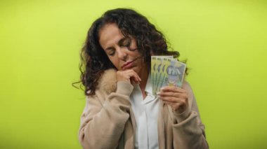 Elinde banknotlar tutan Romen kadın, parlak sarı izole bir geçmişe karşı düşünceli bir tutum sergiliyor ve mali tefekkür veya karar verme sürecini öneriyor.