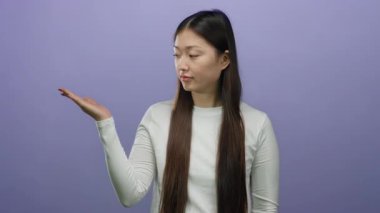 Uzun saçlı, beyaz gömlekli, mor arka planda el kol hareketi yapan ve parmak işareti yapan bir kadın..