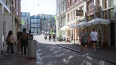 Güneşli bir Avrupa caddesinde bulanık şehir manzarası. Odaklanamayan yayalar ve binalar. Odaklanamayan ışık ve gölgelerle sakin bir kentsel atmosfer yaratıyor..