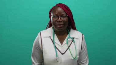 Yeşil arka plana güvenerek gülümseyen kadın steteskop takıyor, profesyonellik duygusunu ve sıcaklığını izole bir ortamda aktarıyor..