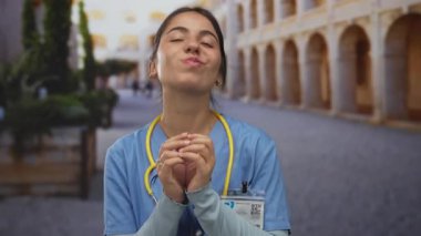 Steteskoplu mavi üniformalı gülümseyen kadın doktor tarihi eski kasabada duruyor, mesleki güven ve yerel çekicilik sergiliyor..