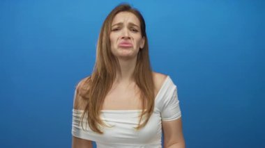 Beyaz omuzlu genç bir kadın dudaklarını büzüyor ve mavi stüdyo setinde yüzüne yumruk atıyor. Üzüntü..