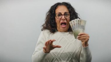 Elinde Mısır banknotları tutan orta yaşlı bir kadın izole edilmiş beyaz bir arkaplan karşısında şok olmuş gibi görünüyor, Mısır 'dan gelen para birimiyle anlamlı bir anı yakalıyor..