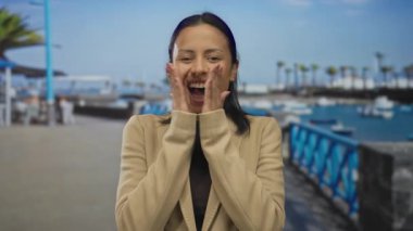 İspanyol kadın açık deniz limanında sevinçle gülümsüyor tekneler görünürde, bir sahile karşı el çırpıyor mutluluk ve sükunet hissi yaratıyor..