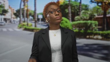 Siyah ceketli kadın şehir sokağında arka planda bulanık palmiye ağaçları olan tapınağı işaret ediyor. Düşünceli bir yansıma..