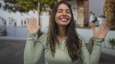 Çevresinde ağaçlar ve geleneksel mimari bulunan büyüleyici kentsel alanda gülümseyen genç bir kadın, toplum ortamında mutluluğu ve gündelik modayı somutlaştırıyor.