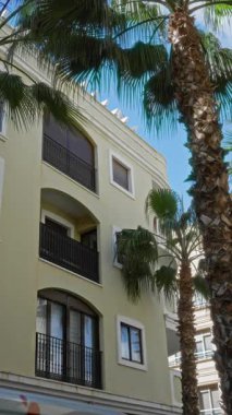 Açık mavi gökyüzünün altında, Torrevieja, İspanya 'da balkon ve palmiye ağaçlarıyla ön cephe inşa ederek, Akdeniz mimarisi ve açık hava manzarasını ön plana çıkarıyor..
