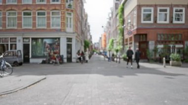 Amsterdam 'daki Bulanık Sokak Sahnesi' nde yayalar tuğla binaların önünden geçerken canlı bir şehir atmosferi yaratıyor..