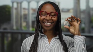 Bir kadın açık şehir ortamında elinde ethereum sikke tutarken gülümsüyor kripto para birimi ilgisini ve modern finansal eğilimleri gösteriyor.