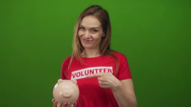 Stüdyoda yeşil duvarlı seramik domuz kumbarasını işaret eden gönüllü bir kadın..