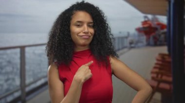 Kıvırcık saçlı Latin kadın parmaklıkların yanındaki güneşli tekne güvertesinde kendini işaret ediyor..