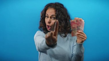 Öfkeyle el kol hareketi yapan bir kadın, Güney Afrika banknotlarını mavi duvara dayayıp para durumuyla ilgili hayal kırıklığını gösteriyor..