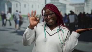 Steteskop hareketleriyle Afro-Amerikalı kadın tamam ve kalabalık bir şehir caddesinde elini gösteriyor..