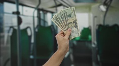 Bir otobüs vitrininde dolar tutan Amerikalı adam el, banknotlar ve kapalı alanda toplu taşıma ortamında ABD para birimini vurguluyor..