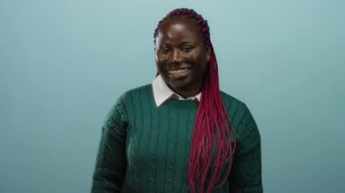 Yeşil süveter giymiş, mavi arka planda sırıtan, neşe ve sıcaklık saçan bir kadın..