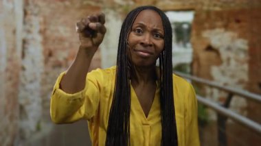 Antik Roma harabelerinde kıvırcık saçlı bir kadın sarı bir gömlek giyerken tarihi bir mekanda düşünceli bir anı yakalıyor..