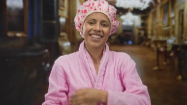 Pembe bornozlu ve duş boneli genç İspanyol kadın müzede gülümsüyor, kültürel keşiflerle günlük rahatlığı harmanlıyor.