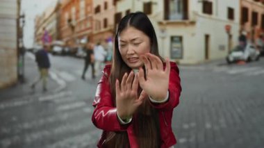 Kırmızı ceketli bir kadın şehir sokaklarında hareketsiz duruyor. Geçmişi bulanık, hayat dolu ve yürüyen insanlar var..