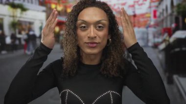 Altın halkalı küpeli transseksüel kadın hareketli bir şehir caddesinde iki elini birden kaldırıyor..