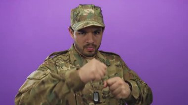 Kamuflaj üniformalı genç adam stüdyoda yumruğunu kaldırıyor ve künyesini tutuyor. Kararlılık görevi hazır olma cesareti..