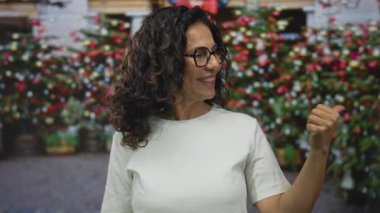 Beyaz gömlek giyen orta yaşlı İspanyol kadın sokakta başparmağıyla işaret ediyor; güveni yönlendirme pozitifliği.