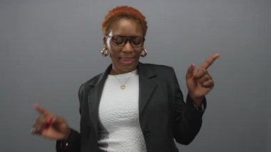 Gözlüklü ve spor ceketli bir kadın sunum için stüdyoyu işaret ediyor..