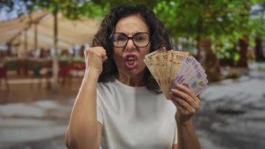 Orta yaşlı Meksikalı kadın, elinde peso banknotların hayranı, öfke bunalımı yaşıyor..