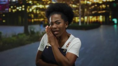 Önlüklü kadın geceleri şehir caddesinde gizli şeyler fısıldıyor. Arka planda parlak ışıklar, canlı bir şehir ortamı yaratıyor. Entrika hissini iletiyor..