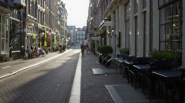 Amsterdam 'daki odaksız sokak görüntüsü, güneşli bir günde kafelerin dışında oturan bulanık insanları Avrupa mimarisinin Hollanda kentsel ortamını vurguluyor.