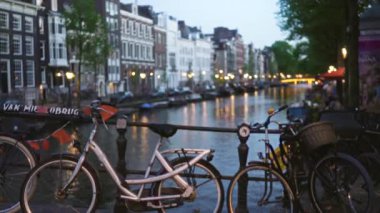 Arka planda tarihi binalar bulunan Hollanda 'nın büyüleyici akşam manzarasını aydınlatan odaksız Bokeh ışıklarıyla pikoresk bir kanal boyunca park edilmiş bisikletler..