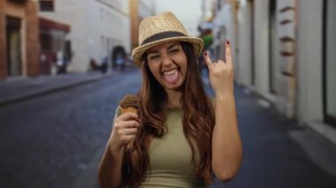 İspanyol kadın güneşli bir caddede dondurma yiyor, taş jestler yapıyor, hasır şapka ve yeşil tişört giyiyor, mutluluk ve pozitiflik saçıyor..