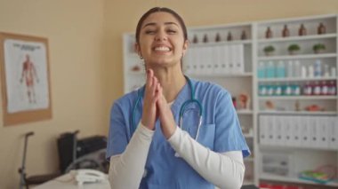 İspanyol üniformalı kadın hemşire hastane odasında sevinçle gülümsüyor. Arka planda tıbbi ekipmanlar var. Sıcaklık ve profesyonelliği yansıtıyor..