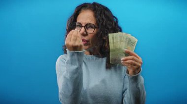 Arjantin pesolarını mavi bir duvara karşı öfkeyle tutan kadın banknotlar eline yayılmış, hayal kırıklığı ve yoğunluk yayıyor..