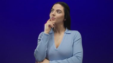 Parlak mavi bir arka plan üzerine kafa yoran, açık mavi bir bluz giyen, düşünceli bir ifadeyle, düşünceli bir düşünce, gençlik, kendine güven ve modernliği somutlaştıran bir kadın.